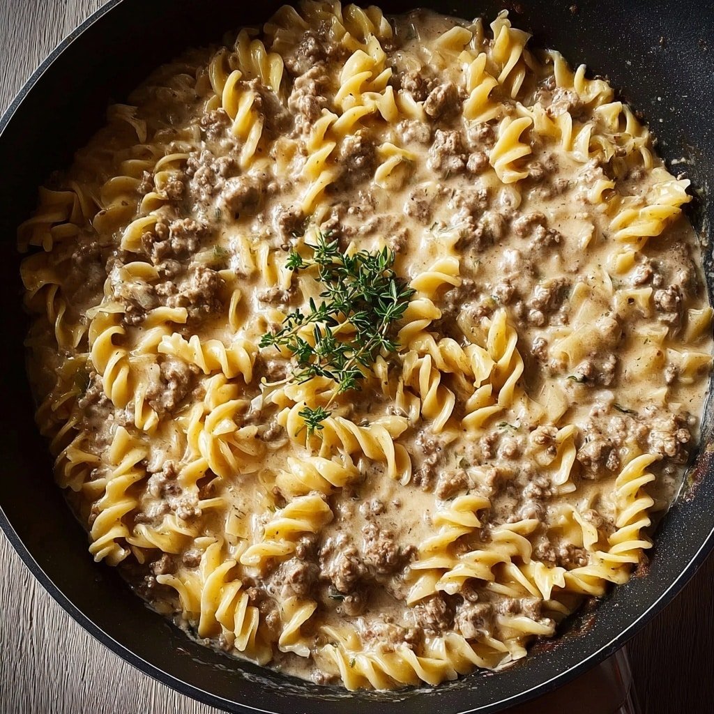 This dish shows a deep bowl filled with wide, light yellow egg noodles as the bottom thick layer, topped with a creamy sauce mixed with small, cooked brown pieces of ground meat in the middle layer. Green chopped herbs are sprinkled evenly over the top layer, adding a fresh contrast. Thin cheese shreds are lightly spread around throughout the sauce layer. The bowl rests on a white marbled surface, and the close view highlights the texture of the noodles and creamy sauce photo taken with an iphone --ar 1:1 --v 7 — Ground Beef Stroganoff, creamy beef stroganoff recipe, easy beef stroganoff, comfort food dinner, quick weekday meals